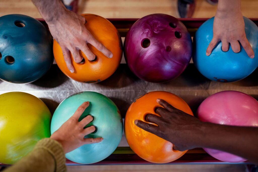 Unrecognizable Bowling Players Selecting Balls in Indoor Alley